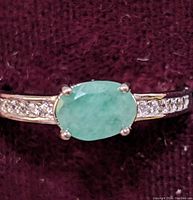 Close-up image of the ring showing oval green emerald center stone with cubic zirconia stones on sterling silver band.