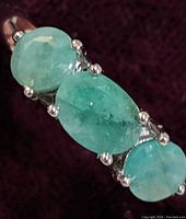 Close-up front view of the sterling silver ring with three emerald stones showing the oval center stone flanked by two smaller round stones.