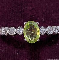 Close-up front view of sterling silver ring with oval green peridot and six round cubic zirconia stones on the band.
