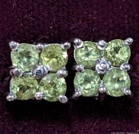 Close-up front view of the pair of sterling silver earrings with four square peridot stones on a dark background.