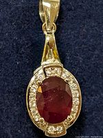 Front view of sterling silver pendant showing oval deep red gemstone surrounded by small clear stones on dark blue background.