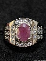 Front view of sterling silver ring showing oval ruby surrounded by cubic zirconia stones arranged in a rectangular pattern with a grid on the band shoulders.