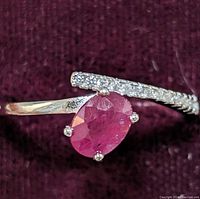 Close-up front angle of the sterling silver ring showing the oval red ruby and the cubic zirconia stones on the curved band.