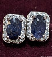 Close-up front view of sapphire and cubic zirconia stud earrings on a dark red fabric background.