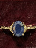 Close-up front view of sterling silver ring featuring oval blue sapphire and cubic zirconia accents on the sides and band.