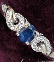 Close-up of the sterling silver ring showing an oval sapphire center stone with cubic zirconia accents on the band.