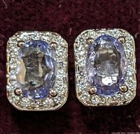 Close-up front view of the pair of sterling silver earrings showing the oval tanzanite stones surrounded by a halo of cubic zirconia stones.