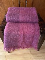Folded fuchsia and deep rose mohair blanket with fuzzy texture, laid over a chair showing fringed edges.