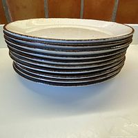 Stack of 10 dinner plates showing the burnt cinnamon rim and speckled cream surface.