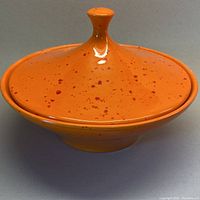 Front view of the bright tangerine ceramic lidded serving dish with red speckles, showing the knob handle on the lid and the flared base.