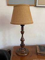 Full view of wooden table lamp with beige sandy burlap shade on wooden surface against cream wall