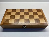 Closed rectangular wooden folding chessboard with inlaid checkered pattern in two wood tones, showing latch on front side.