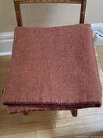 Blanket neatly folded over a wooden chair showing its mottled cinnamon wool texture and hand-stitched edges.