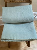 Folded light mint green wool blanket on wooden chair, showing size and thickness.