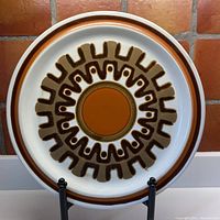Full view of the round chop plate showing cream background with brown and orange Aztec-inspired design.