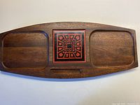 Top-down view of entire hardwood cheeseboard showing two indentations and central ceramic tile with geometric pattern.