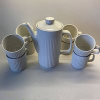 Front view showing all 8 ribbed white ironstone mugs and central hot chocolate pot with lid and spout.