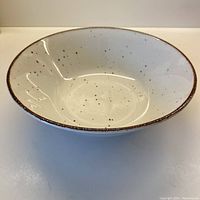 Front side view of ceramic serving bowl showing the cream background with cinnamon speckles and burnt cinnamon rim.