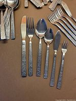 Photo showing a set of knives, forks, spoons, small forks, and spreaders with raised floral detailing on the handles.