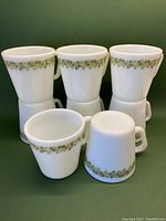 Five of the eight white milk glass coffee mugs arranged upright and one tipped to show the floral pattern and shape.