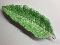 Top and side views of the ceramic leaf-shaped serving bowl showing detailed textured veins and glossy finish.