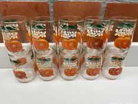Front view of 10 vintage juice glasses arranged in two rows, showing orange fruit and green leaf design on each glass.