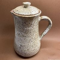 Front view of the lidded ceramic pitcher showing the full body and lid with cinnamon speckled cream glaze.