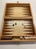 Top view of open wooden backgammon case showing playing board, dice and pieces.