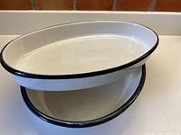 Two white enamelled oval metal pans with black rims stacked inside each other showing dimensions and condition.