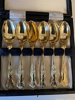 Six silver plate teaspoons with ornate handles displayed inside a velvet-lined presentation box.