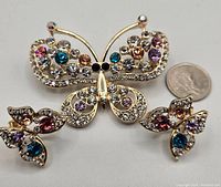 Butterfly brooch and earrings laid flat with quarter for size comparison showing multicolored Austrian crystals and gold-tone metal.
