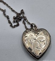 Close-up of the heart-shaped sterling silver locket showing detailed floral engraving on the front.