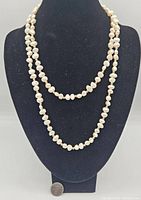 Front view of the freshwater pearl necklace displayed on black necklace stand with a coin for size reference.