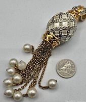 Close-up photo of the bottom tassel detail showing gold-tone chains ending with faux pearl drops, alongside a quarter for size comparison