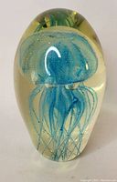 Photo showing clear glass paperweight with blue jellyfish design inside.