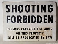Photo of a vintage metal sign with the text 'Shooting Forbidden' clearly visible. The sign is white with black text and shows some signs of age.