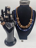 Photo showing two bead necklaces and bracelets displayed on black stand and hand with rhinestone accents