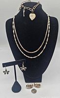 Front view of displayed necklaces, bracelet, and earrings on black mannequin stand and earring holder showing size and style