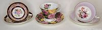 Front view of three tea cups with matching saucers, each with different floral patterns and gold trim.