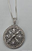 Front view of the round sterling silver pendant showing white stones in filigree design.