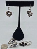 Photo showing all three pairs of sterling silver earrings including heart-shaped, purple stone, and black stone pairs, with a quarter for scale.