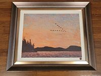Framed print showing a lakeside sunset landscape with birds and signature seal.