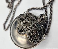 Close-up of the ornate vintage Tibetan stone set perfume bottle pendant, showing decorative filigree and black stones with one stone missing.