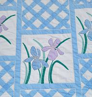 Close-up photo showing floral patch with purple and blue flowers and green stems, detailed stitching visible.