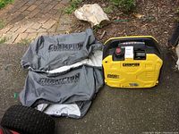 Photo of generator and two gray Champion branded covers on ground, generator is yellow and black with model markings visible.