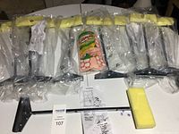 Nine packaged window squeegees with yellow handles and attached wash sponges, along with one Wonder Mop refill and some instructions laid out on a white surface.