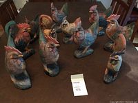 Photo of eleven hand-carved wooden chicken figurines with faded multicolor paint placed on a wooden table.