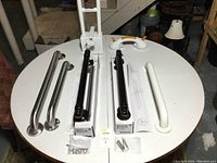 Photo showing 6 different grab bars on a round table, including 2 stainless steel, 2 oil-rubbed bronze Koehler bars, 1 white coated bar, plus a bathtub grab assist and suction cup grab bar.