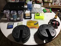 Wide view of the camping gear laid out on a white round table including tent weights, drink tumblers, ice gel packs, safety vest, rubber foam strips, poly rope, and other small items.