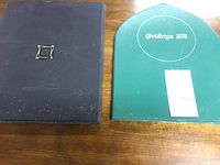 Two hardcover stamp books laid on a wooden surface, one green labeled 'Christmas 1978' and one dark blue with a square emblem on the front.